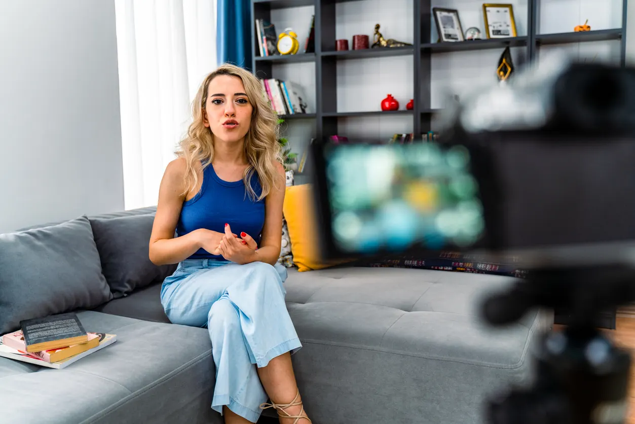Gri kanepede oturan sarışın bir kadın karşısındaki kameraya konuşarak video çekiyor