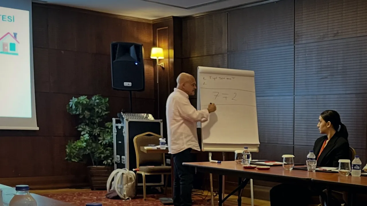 Güven Açık kâğıt tahtaya yazıyor; tahtada “Fiyat son mu?” sorusu var