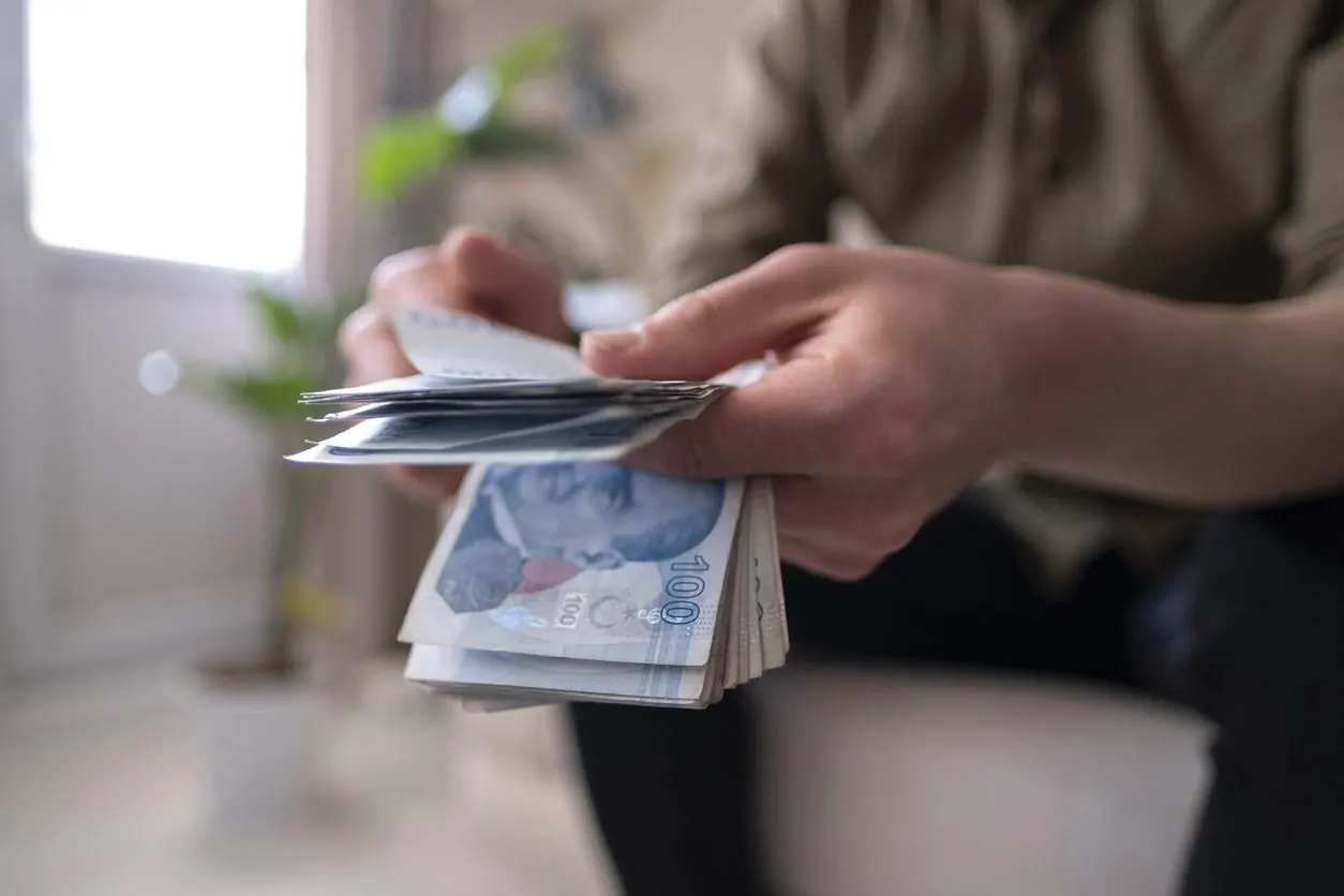 Elindeki 100 Türk lirası banknot destesini sayan bir kişinin elleri