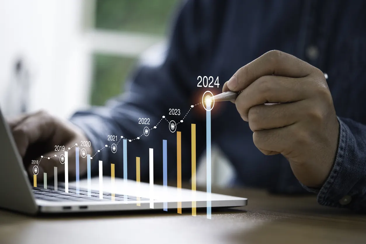 Dizüstü bilgisayar başındaki kişi, 2018’den 2024’e yükselen sütun grafiğinin son sütununu kalemle işaret ediyor